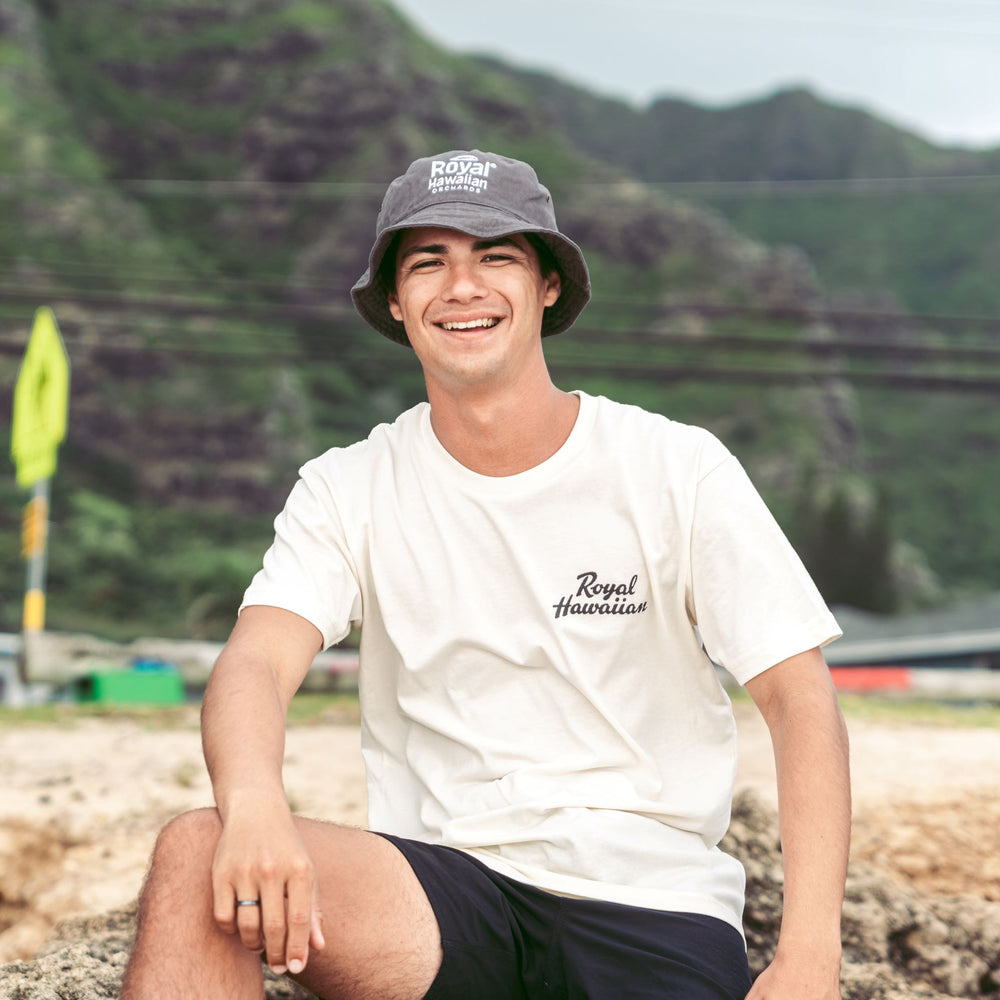 boy sitting on beach wearing gray bucket hat with royal hawaiian orchards logo
